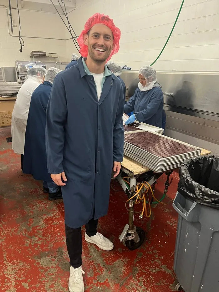 David in a hairnet and lab coat beside trays of Nebula chocolate bites on the production floor