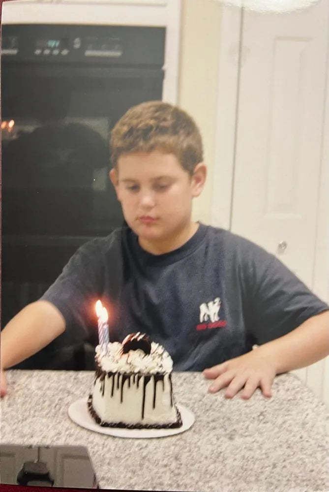 Young David at a birthday, looking at a small chocolate-drizzled cake